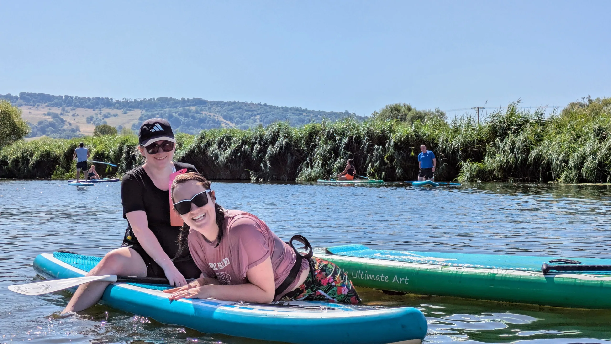 Two friends half in, half out of the water laughing near their paddleboards